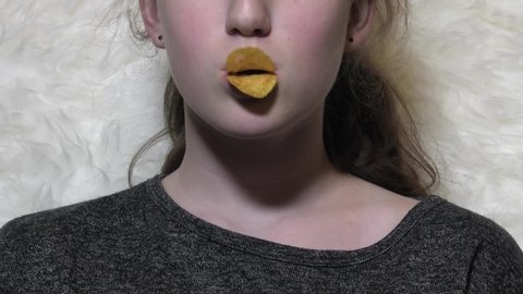 Young little caucasian child girl eating crispy potato chips and makes duck lips out of chips, naughty.