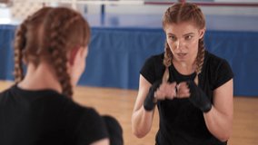 Close-up demonstration video of a young attractive professional female boxer training in front of mirror. Physical exertion in sport concept