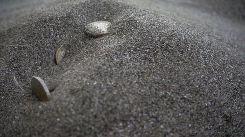 Slow motion euro coins fall and burrow into a pile of sand.