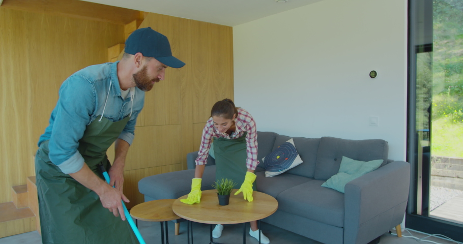 Positive smiling professional cleaners doing cleanup in ordinary apartment.