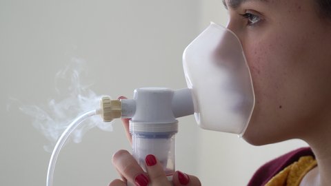 Young woman doing inhalation nebulizer in hospital, holding a mask nebuliser inhaling asthma and bronchitis medication to improve breathing. Healthcare, medicine, care, flu, disease concept.