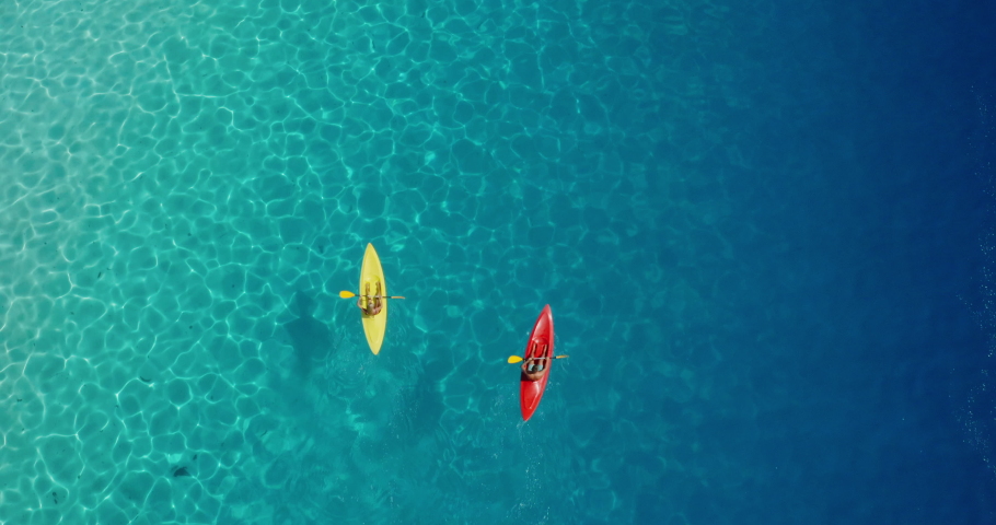 Aerial view of adventurous couple ocean kayaking together in pristine blue lagoon with sunny light textures refracting on the water surface, leisure kayaking tourism
