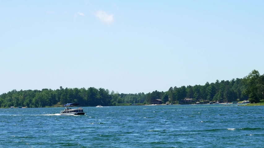 Pontoons on a beautiful lake in northern Minnesota with blue sky and fluffy clouds. Boating in Minnesota, Land of 10000 Lakes.