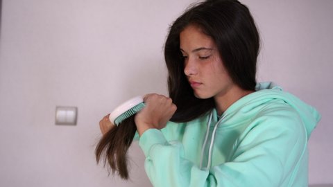 young angry brunette teenager in turquoise hoodie combs long hair and throws away hairbrush screaming closeup