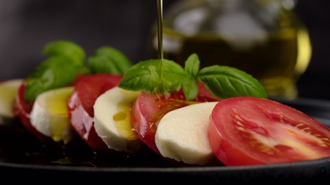 cook pouring olive oil on a Italian salad caprese. tomatoes, mozzarella, basil leaf. 