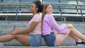 Attractive multiethnic females sitting back on university stairs, friendship