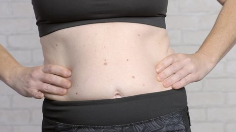 Excess fat in waist of woman. Woman pulls flabby skin with hands from abdomen and back.