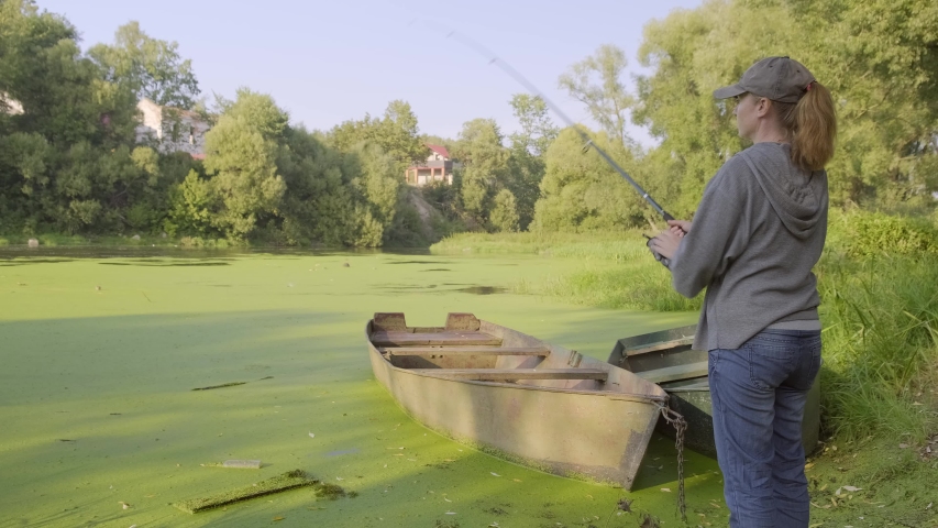 female fishman catches fish on river. Woman fisherman throws  fishing rod into water of river.