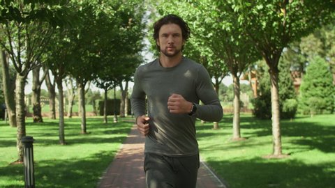 Attractive man, guy jogging in the park on a background of trees, fitness watch