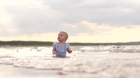 Toddler baby girl crawls in shallow waterline of Baltic sea beach shore enjoy play in water