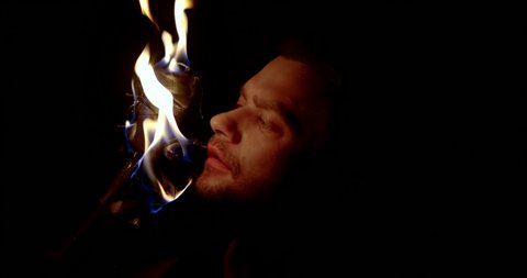 closeup view of male face illuminating two flaming torches in darkness, he is watching flame
