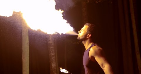 man is breathing on flaming torch for performing trick on fire show in night time