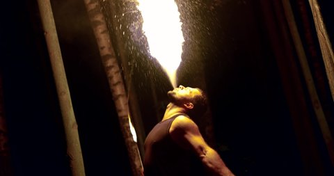 man is breathing fire in darkness, performing famous circus trick