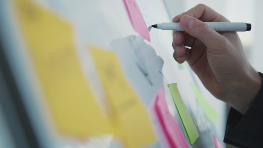 American creative designer writing notes on white board standing in office room. Concept create ux design for people. Young male manager working on new blueprint, taking color notes holding marker in Royalty-Free Stock Footage #1036503749