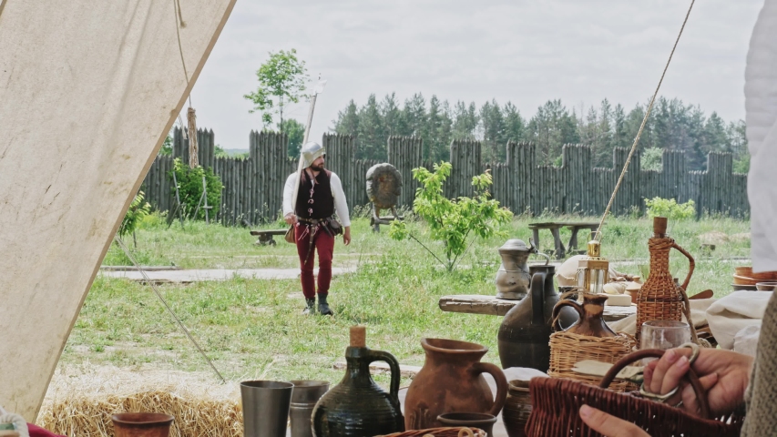 Medieval knight with hammer coming to sitting woman at teepee and take to drink a cup with water