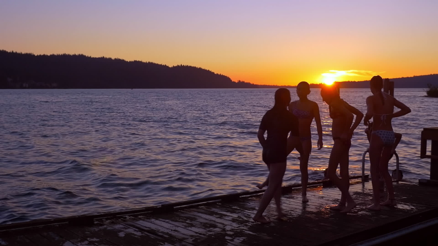 Teenagers jumping from dock into lake at sunset