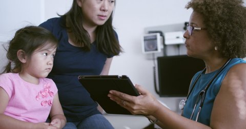 Pediatrician with digital tablet talking to mother and daughter