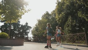 Slow-motion tracking video: Two young girls rollerblading in a city park on a sunny day