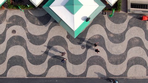 Top-down aerial view of people walking on the iconic Copacabana Beach mosaic sidewalk in Rio de Janeiro, Brazil.