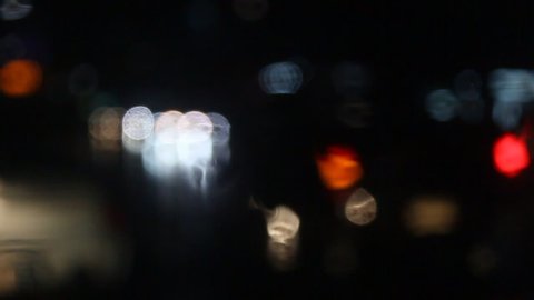 Rain water drops Falling Down On the Windscreen in slow motion, Rain Drops On The Windows Glass, Defocused Night City Traffic Lights. Color Blurred bokeh of moving transport and typical city noise.