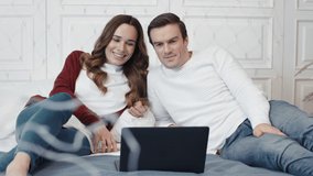 Happy couple watching movie on laptop computer at home together. Smiling family relaxing in front of laptop screen in living room. Cheerful people looking video in notebook in luxury house.