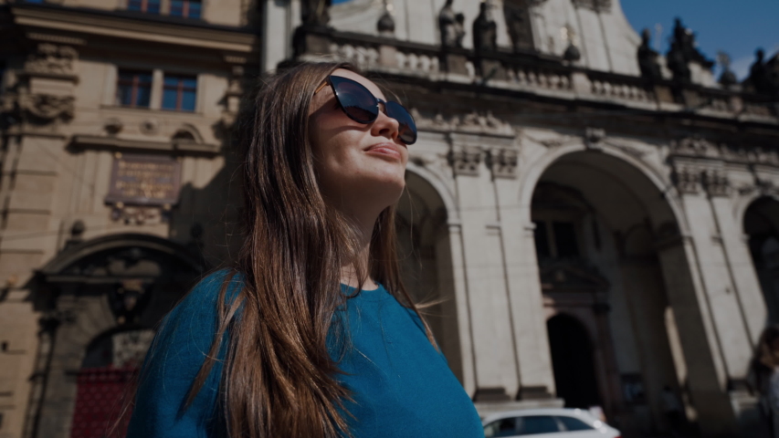 beautiful girl in sunglasses stands in square and looks around on background of historic baroque building in close-up