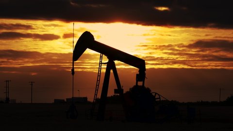 Pump jack. Oil well, close up.Silhouette of an oil pump jack on rig as the sun sets in the background. An oil pump jack on the middle of the wheat field with the beautiful sunset sky. 