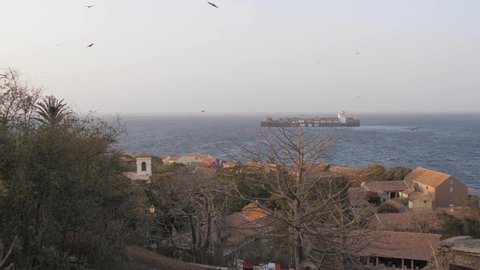 Dakar / Senegal - 03 30 2019: Senegal’s Ile de Gorée ("Slave Island") with a large container ship passing by in the background at sunset