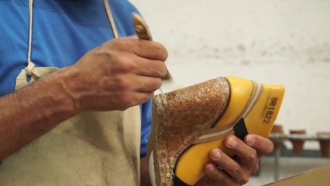 Static shot of a shoemaker brushing glue on a heel before covering it with stitched fabric in a shoe workshop factory