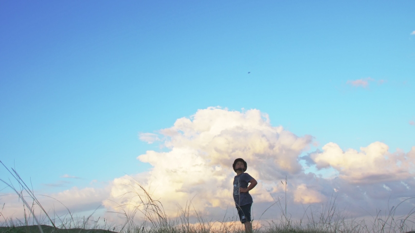 a boy in a motorcycle helmet stands on top of a hill on a background of clouds illuminated by the sunset rays