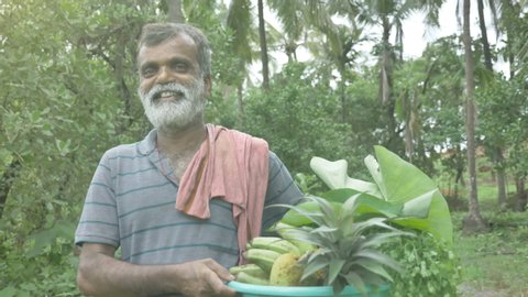 A happy and smiling middle aged bearded male farmer is smiling and looking at the camera with a harvest of vegetables and fruits from the farm.