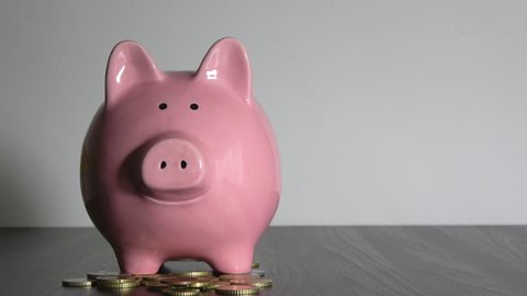 Piggy bank standing on a pile of coins. A hand is putting coins in a piggy bank in concept on a light gray background. Saving money is an investment for the lifestyle of the future. Bank investment.