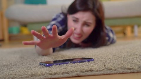 A young woman in a shirt had a heart attack and she tries to reach the smartphone lying on the floor slow mo