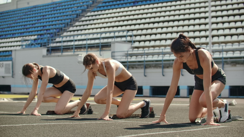 Female runners at athletics track crouching at the starting blocks before a race. In slow motion
