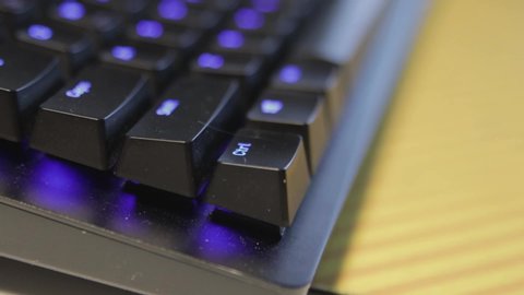 Hand pressing a single key on a slightly dusty, black keyboard with blue backlit keys.