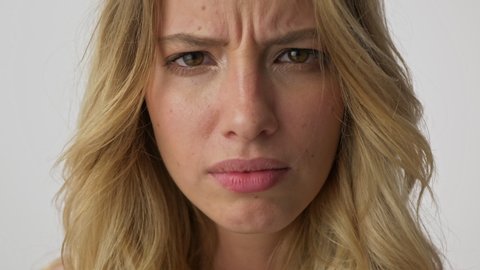 Cropped view of displeased young blonde woman becoming disgusted and grimacing while looking at the camera over gray background isolated