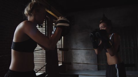 Medium shot of two young female boxers in gloves fighting inside boxing ring