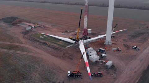 Building process of wind energy power tower mill, under construction. Assembling blades, turbine, rotor. Green, clean, renewable energy. Aerial footage.