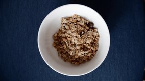 Macro view of healthy diet breakfast of cereal being put in white bowl or plate with spoon, it's placed on table with dark-blue table-cloth. Vertical video frame 9x16.