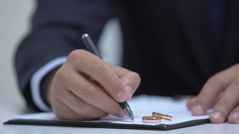 Lawyer writing marriage contract, two wedding rings lying on document, divorce