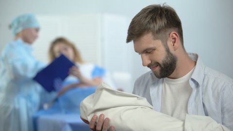 Happy father holding newborn child during nurse explaining wife postnatal care