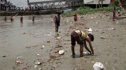 Calcutta / India - 08 09 2019: People wash themselves in the polluted River Ganges in Kolkata. A young boy in the foreground collects mud