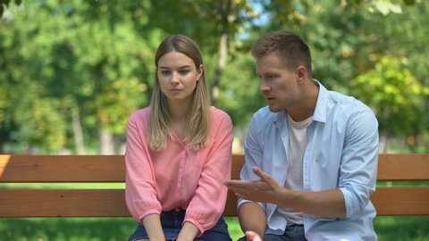 Offended woman listening guilty boyfriend explanations at park after quarrel