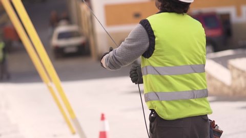 Slow motion shot of a technician worker pulling down an optical fiber cable from a roof of a building with another technician blurred in the background