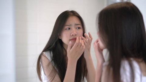 Young beautiful asian woman look at mirror problem acne on face her strain after wake up in the morning in bathroom 4k resolution.