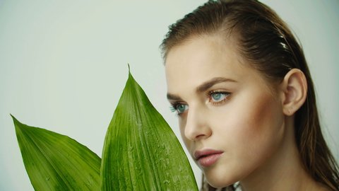 Portrait of young girl with clean smooth skin and with large leaves of plants. Natural and organic cosmetics, skin care. Natural make-up. Girl cover of female face large leaves of plant.