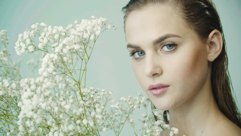Portrait of girl with clean smooth skin, nude makeup against the background of branches of gypsophila plant in studio. Natural and organic cosmetics, skin care, shampoo. Girl posing for camera.