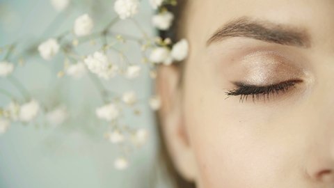 Close-up of girl's eyes with clean smooth skin, nude make-up. Girl's face among gypsophila plants. In studio. Girl opens her eye looking at camera. Vision. Beautiful eye. Half face in frame.