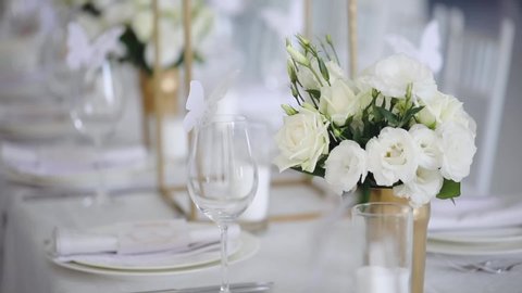 wonderful white table decorations with flower bouquets plates by glasses with butterflies for wedding party slow motion