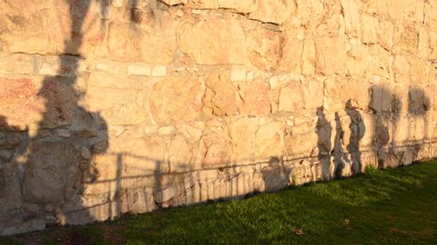 Shadows of people reflected on the wall surrounding the Old City of Jerusalem. Shadows of locals, tourists and religious people walking during a beautiful sunset. Jerusalem, Israel.